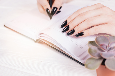 Top view on white wooden table with empty diary and girl's hands with pen, free space. Girl's hands writing in diary. Salon.の写真素材