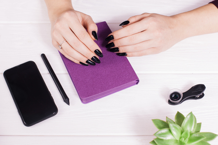 Top view on white wooden table with empty diary and girls hands with pen, free space, black telephone. Salon. Nail scissors. White wooden backgroundの写真素材