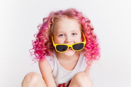Colored wavy hairs. Little modern hipster girl in fashion clothes, smiling. Studio. Isolated on whiteの写真素材