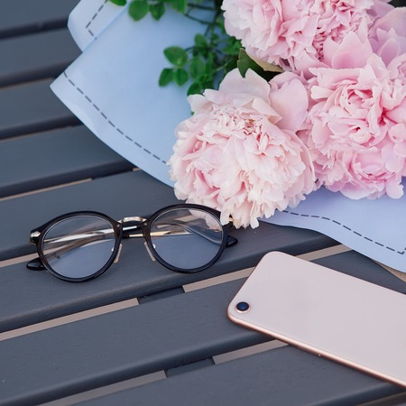 smartphone, spectacles and bouquet of peonies on the wooden table in outdoor restaurant. Work space. Dating, meeting. Romanticの写真素材