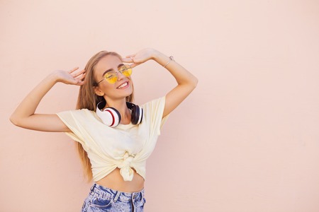 Portrait of beauty fashion smiling young women with yellow sunglasses, wireless headphones, dancing and relaxing. Flying hairs. Outdoorの写真素材