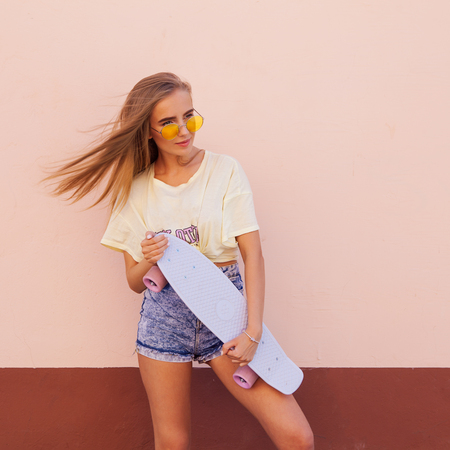 Portrait of beauty fashion smiling young women with yellow sunglasses holding longboard. Flying hairs. Outdoorの写真素材