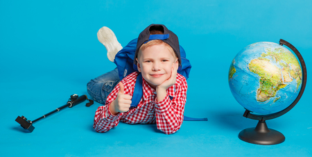 portrait of little funny school blogger boy with action camera and globe. Hipster. concept social networks, education and travel. Isolated on the blue backgroundの写真素材