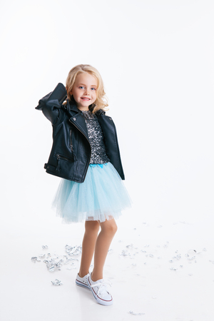 beautiful little girl with curly blonde hairstyle siting on the holiday party in dress with sequins and black jacket. Silver foil on the floor. Concept Celebrationの写真素材