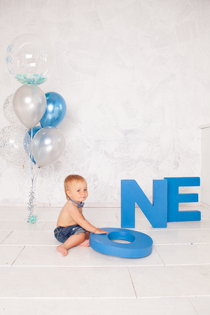 Portrait of fashion funny little boy in studio with big blue letters, balloons and cake. Concept celebrationの写真素材