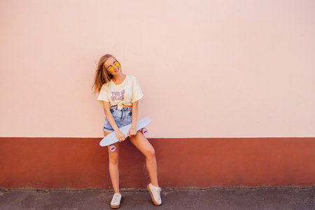 Portrait of beauty fashion smiling young women with yellow sunglasses holding longboard. Flying hairs. Outdoor. Place for text. Concept healthy lifestyleの写真素材