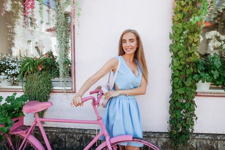 Inspired shapely woman student with pink backpack standing on background with pink bicycle in blue dress. Concept lifestyle.の写真素材
