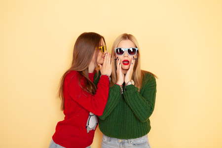 Two funny beautiful hipster girls in sweaters and sunglasses gossiping. Concept winter and fashionの写真素材