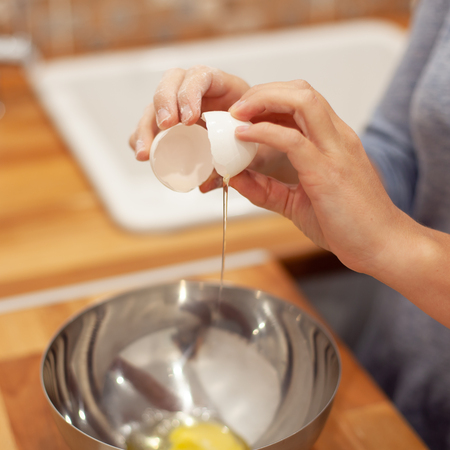 woman breaking the egg in the metal plate and preparing for making the cake in her kitchenの写真素材
