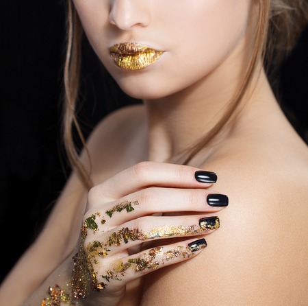 Beautiful Fashion woman model face portrait with gold lipstick and black nails. Glamour girl with bright makeup. Beauty female. Perfect skin and make up. Nail polish. Isolated on blackの写真素材