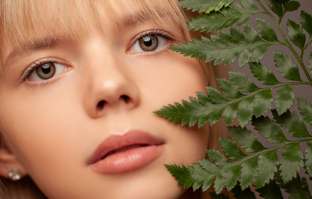 Young woman with fresh healthy skin and hairs holding fern and smiling. Cosmetology, beauty and spa. Grey background. Eyes careの写真素材