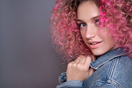 Portrait of beautiful woman with pink curly colored hairs in blue jeans jacket. Glitter makeup. 90s...