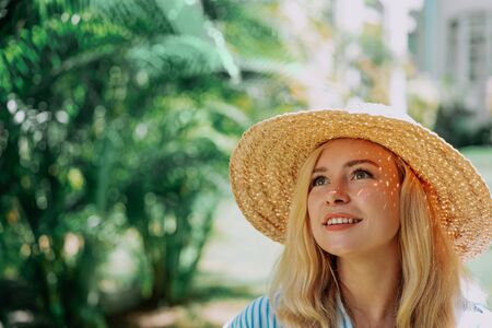 Portrait of beautiful of traveler woman with hat smiling behind palm trees. Sunlight. Concept...