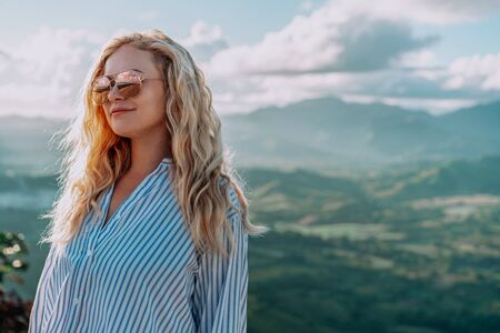 Beautiful view of young woman in sunglasses smiling on the top of the mountain on the dawn. Great...