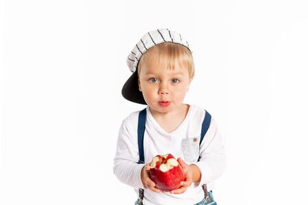 Baby boy eating apple and smiling in the studio isolated on white background. Concept healthy fresh...