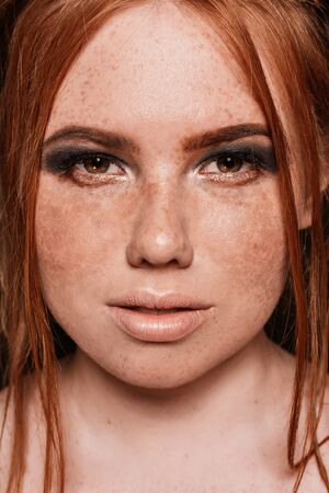 Close-up portrait of beautiful natural woman with freckles on her face and blue glittered smokey eyes make-up. Red hairstyle. Studioの写真素材