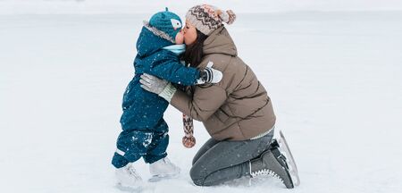 Little funny boy kissing and learning to skate with his mother in the park. Outdoor. Winter sport....