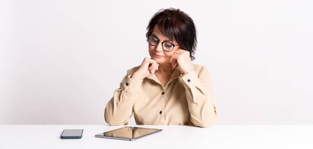 Beautiful Senior woman work at home in glasses and comfortable clothes by smartphone and tablet. Side hustle. Teacherの写真素材