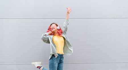Beautiful woman with colored pink hairs and wireless headphones enjoying music over grey background