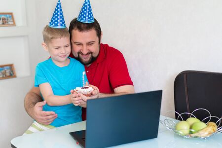 Little boy with his father celebrate birthday online, talking by notebook with relatives and...