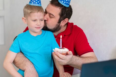 Little boy with his father celebrate birthday online, talking by notebook with relatives and friends. Blow out the candle on the cakeの写真素材