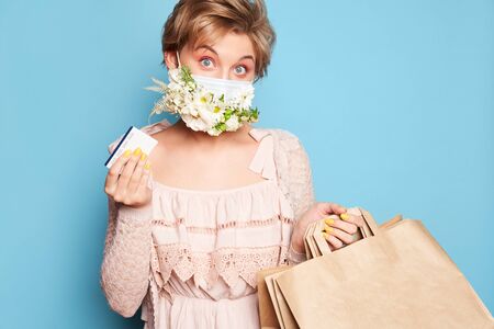 Fashion beauty cool young girl in medical mask designed with natural flowers standing with shopping...