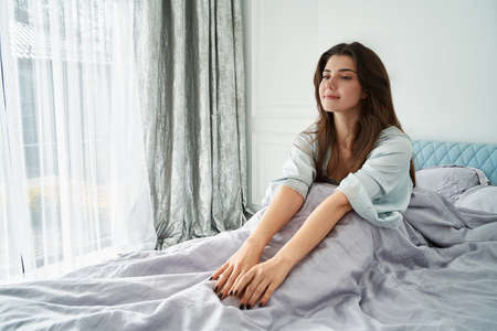 Beautiful woman awake and stretch in comfort bed. Rest, bed linen. Apartmentの写真素材