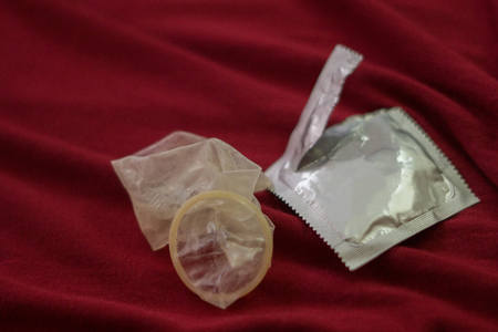Used condom on red bed sheet.の写真素材