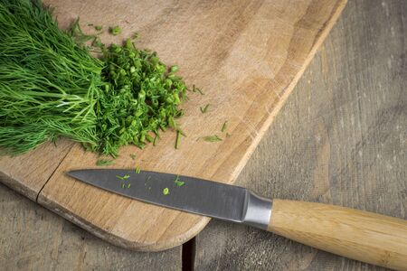 Chopped fresh dill on a cutting Board and a bunch of dill on a wooden backgroungの写真素材