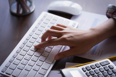 Businesswoman using a calculator for calculating with financial report and  typing on modern computer keyboard at office.Accounting, Finance  and technology in office.の写真素材