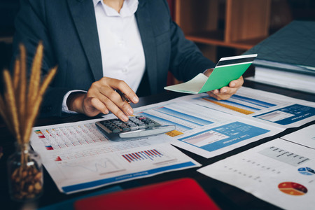 Businesswoman on desk in office using calculator to calculate saving account passbook and statement with financial report .Female accountant or banker use calculator. Savings, finances and economy concept.の写真素材