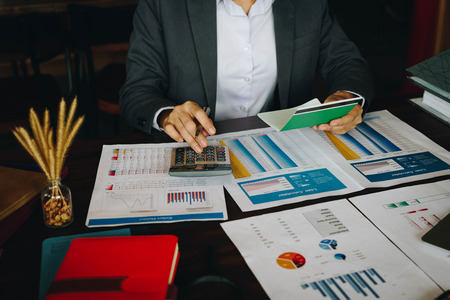 Businesswoman on desk in office using calculator to calculate saving account passbook and statement with financial report .Female accountant or banker use calculator. Savings, finances and economy concept.の写真素材