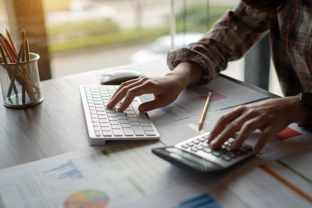 An auditor using a calculator for calculating with financial report and  typing on modern computer keyboard at office. Finance, Accounting and technology in office concept.の写真素材