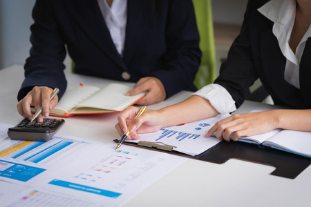 Business woman holding a pen pointing the report and partnership to analyze the marketing plan with calculator on wooden table in office.のeditorial素材