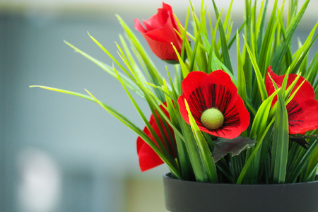 artificial flowers and green leaves in black plastic pot with blurry background