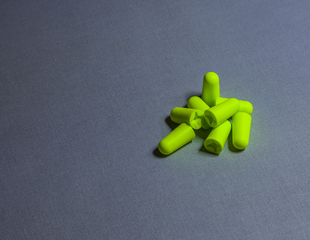 A few small green earplugs on a gray background-image