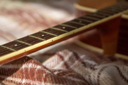 dark neck guitar without strings with frets of light wood on a woolly brown warm cage plaidの写真素材