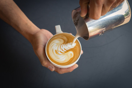Pouring milk from pitcher to cup of coffeeの写真素材