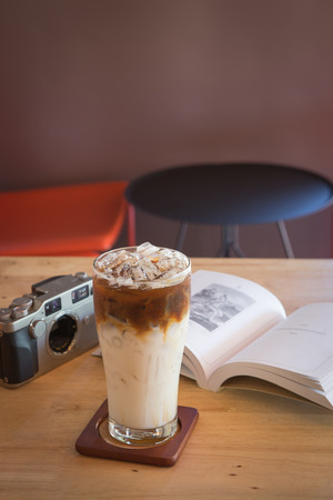 Ice caramel machiato with book and camera on tabel in coffee shopの写真素材