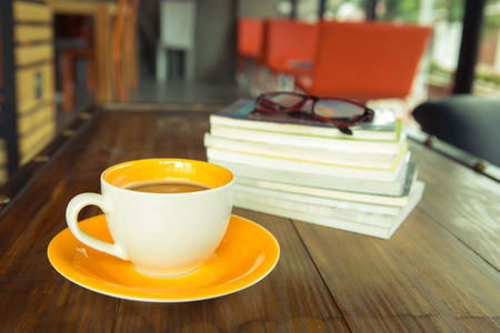 A cup of coffee with books and grasses on wood tableの写真素材