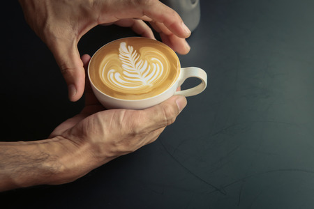 Hold on coffee latte art by Barista on black table