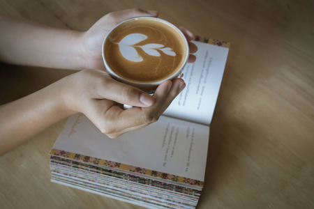 Hand of girl holding cup of coffee  above book after reading.