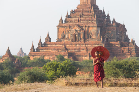 BAGAN, MYANMAR - DEC 13, 2015: novice monk with red umbrella walking around bagan on December 13, 2015 in Bagan, Myanmar.のeditorial素材