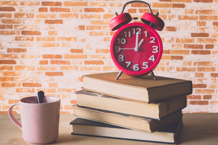 Red alarm clock on old books with cup of coffee on table and brick wall backgroundの写真素材