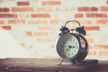 Vintage alarm clock on wood table with brick wall background