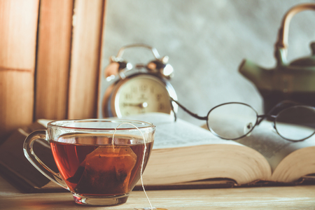 Closeup of reading glasses on the book with tea cup and clockの写真素材