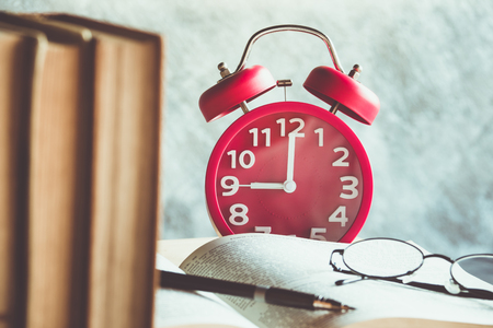 Retro clock with old books and vintage glasses on a wooden tableの写真素材