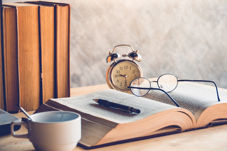 Reading time on wood table with book glasses clock  and cup of coffee or teaの写真素材