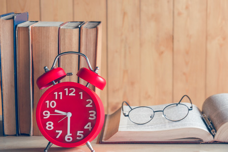 Education concept. Alarm clock with old books and eyeglasses on table . Vintage filterの写真素材