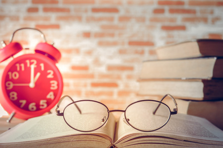 Red alarm clock with book on table and brick wall backgroundの写真素材